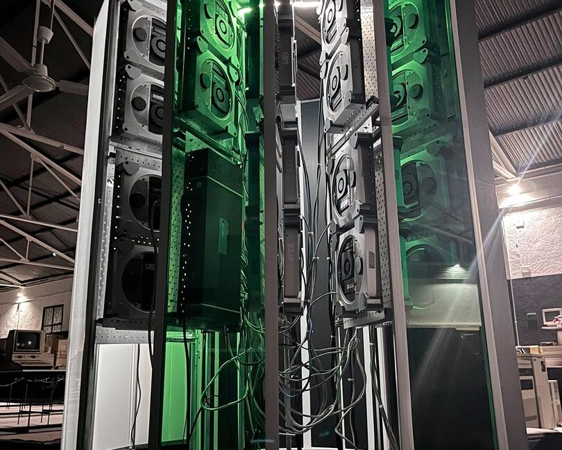 展示 Cray-1 复制品项目尺寸的垂直照片。一个大型 C 形塔架亮起绿色点缀灯光。